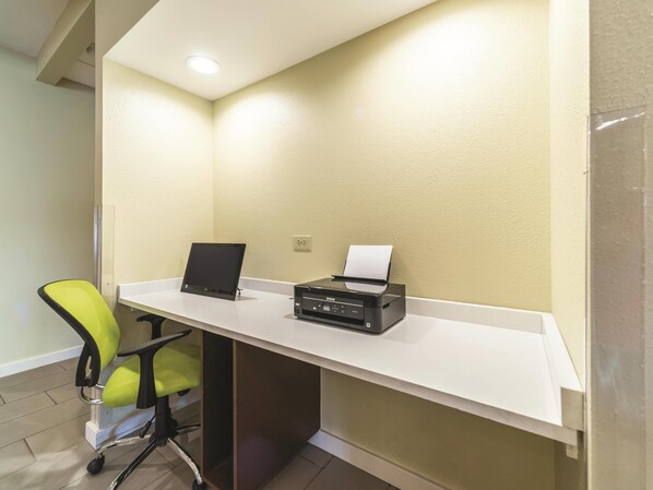 A desk with a laptop and an Epson printer, a green office chair, and a white desk against a textured beige wall.