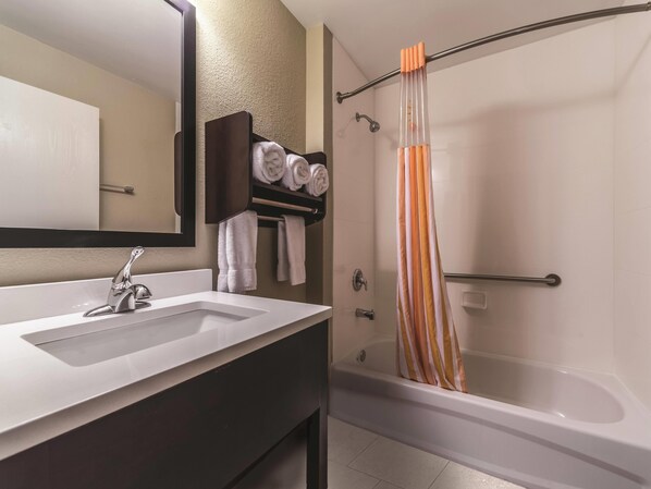 Un baño moderno con un lavabo blanco, tocador oscuro y una ducha con cortina a rayas.
