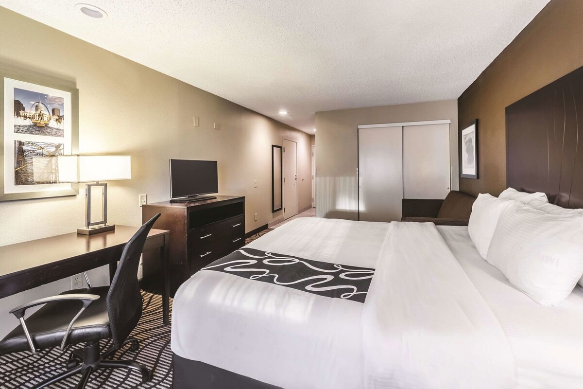 A hotel room with a bed, desk, chair, TV, wardrobe, and a framed picture on the wall.