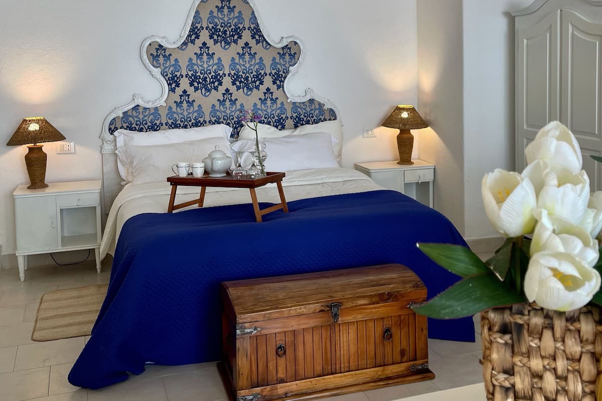 Une chambre avec un grand lit, deux tables de chevet avec des lampes, une commode en bois et un vase rempli de fleurs.