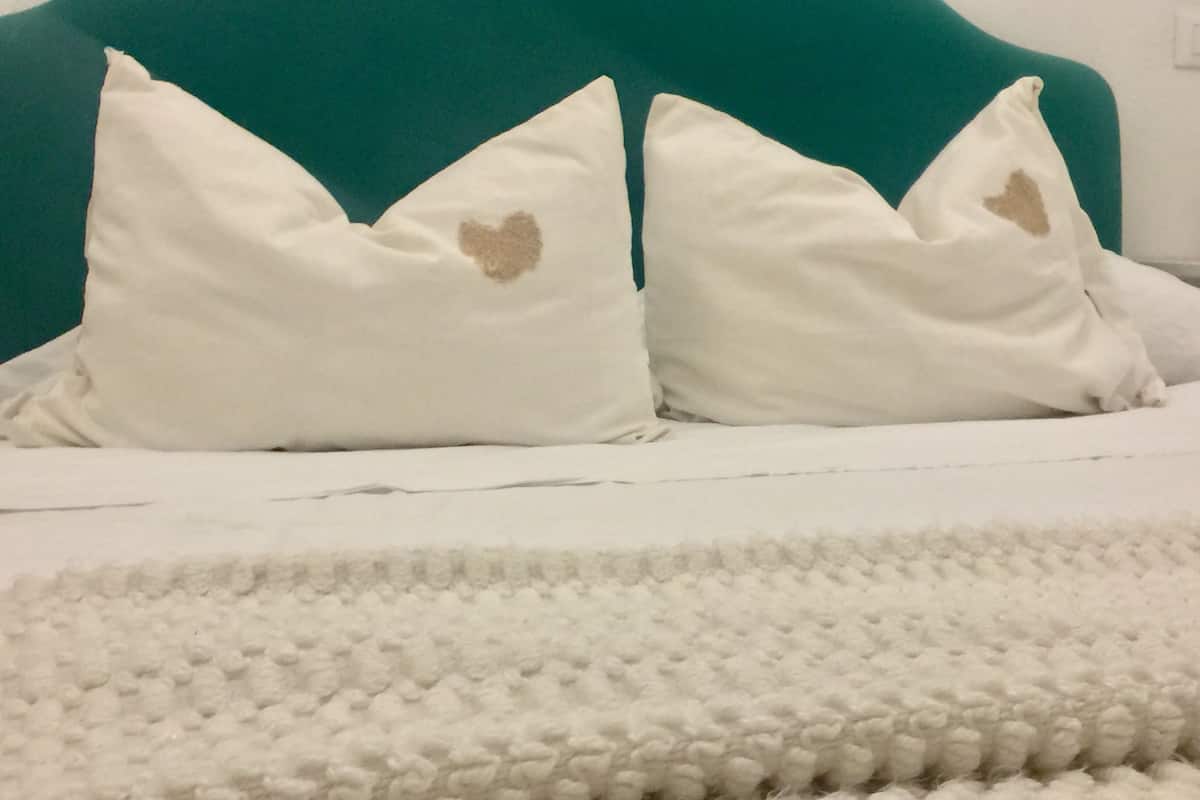 Un lit avec une literie blanche et deux oreillers blancs ornés de motifs en forme de cœur.