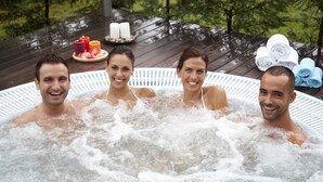 A hot tub with four people, surrounded by candles and towels on a wooden deck. - Balneario Acuña (Caldas de Reis)
