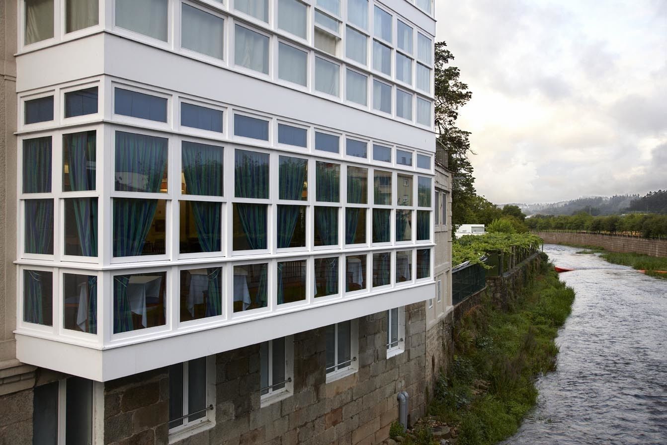 Un edificio moderno con múltiples ventanas y un río al fondo.