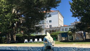 A swimming pool with a water feature, surrounded by lounge chairs and trees. - Balneario Acuña (Caldas de Reis)