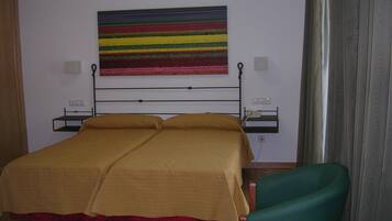 A hotel room with a bed, a green chair, a bedside table, and a colorful striped artwork on the wall.