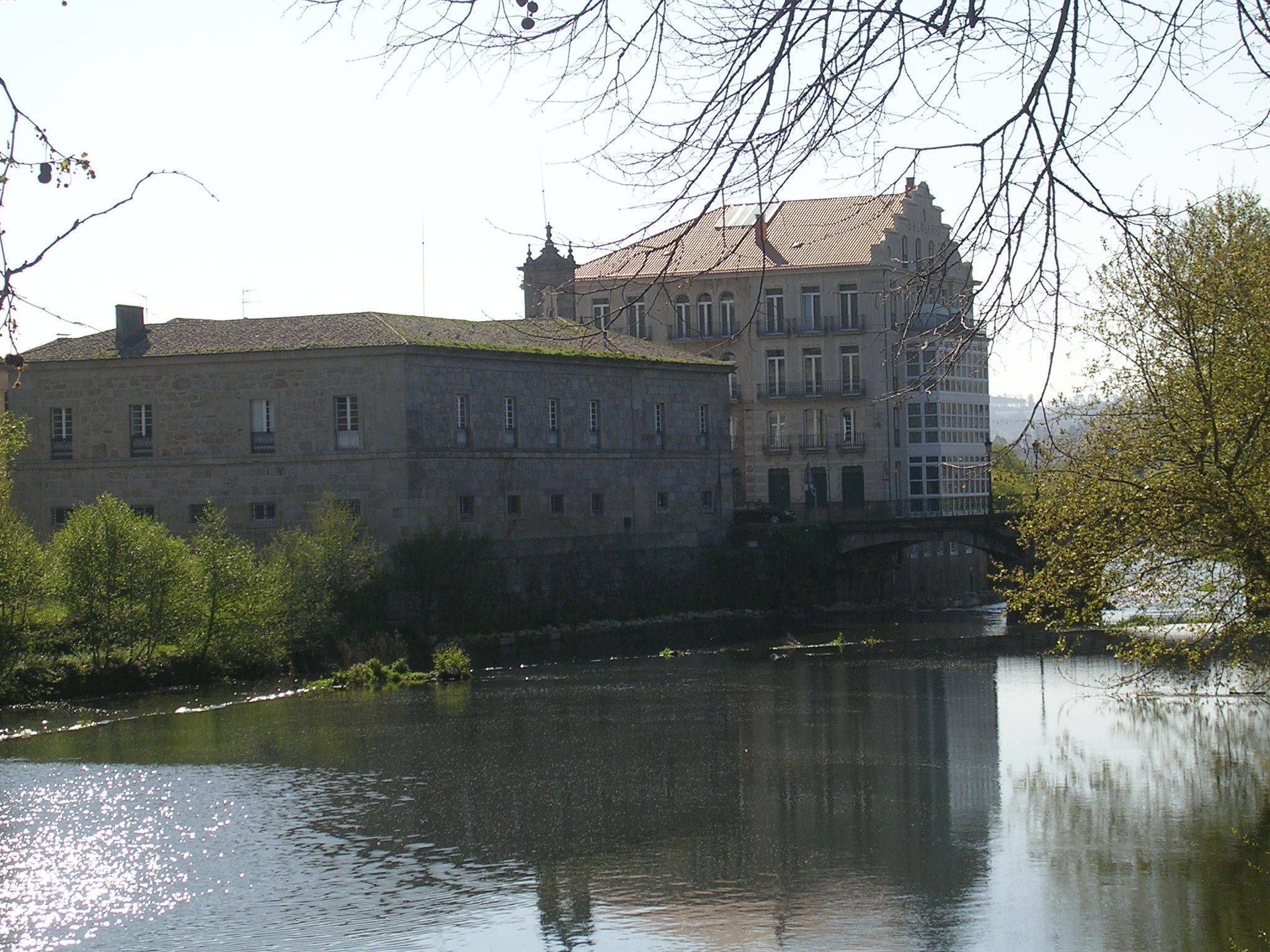 A historic building with a prominent tower, situated by a calm river.