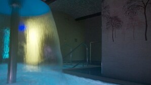 A water feature with a blue light, a pool, and a wall with tree silhouettes. - Balneario Acuña (Caldas de Reis)