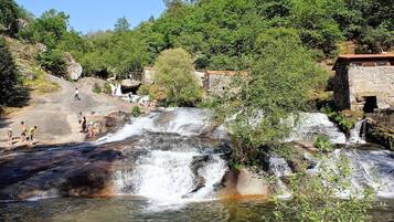 Una cascada con gente a su alrededor, rodeada de vegetación y un edificio de piedra.