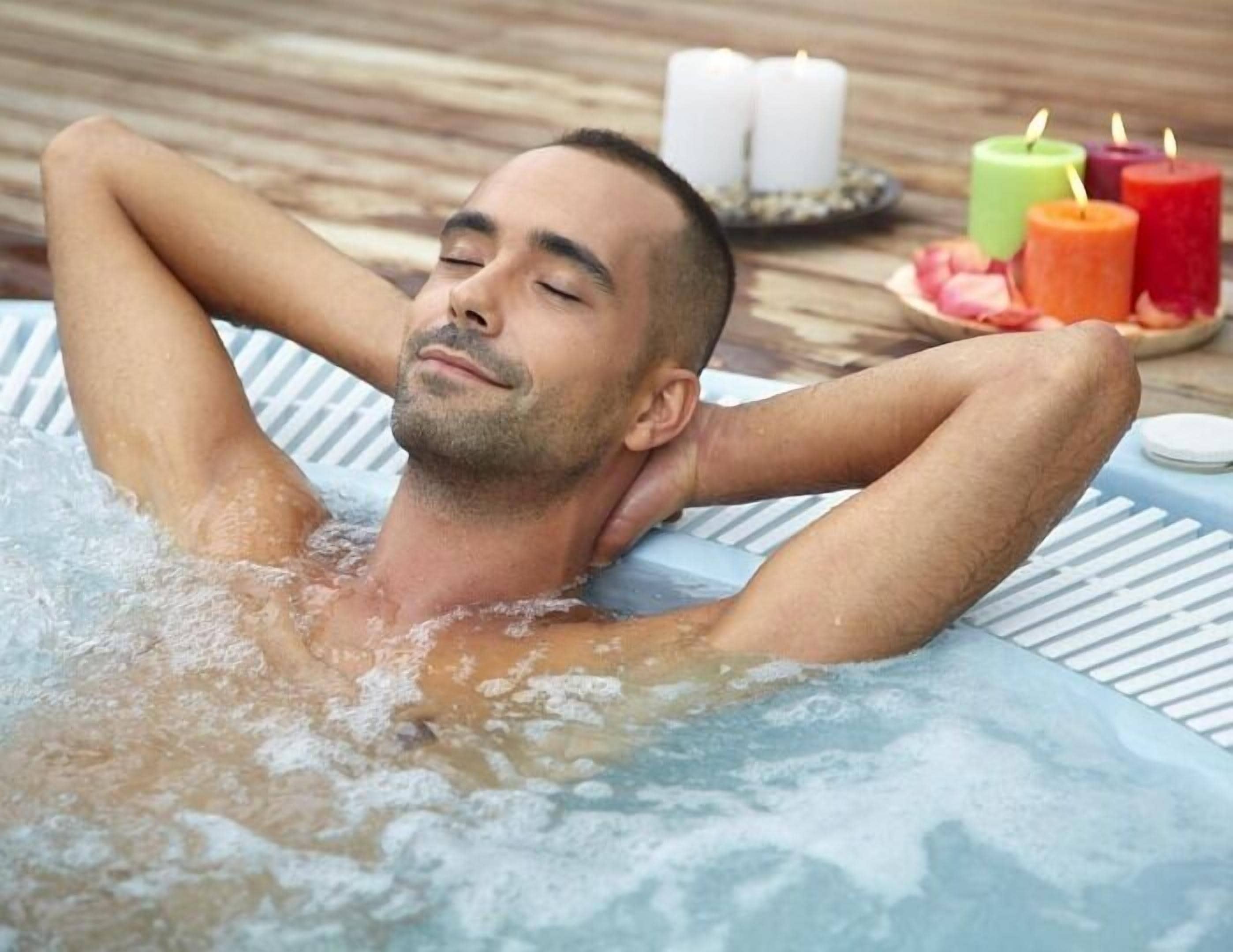 A person relaxing in a hot tub with candles and fruits on the side.