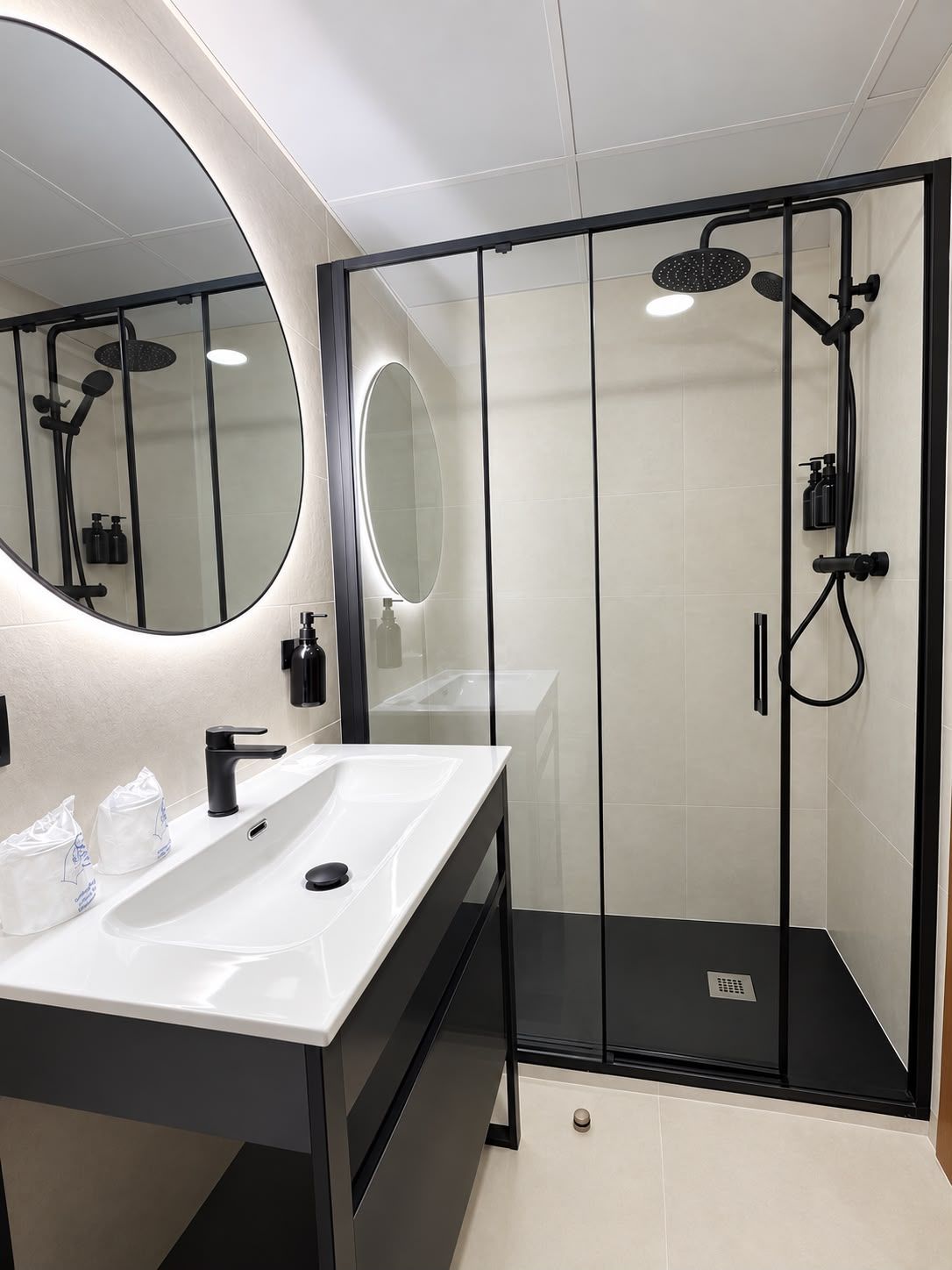 A modern bathroom with a glass-enclosed shower, a large mirror, and a white sink with black fixtures.