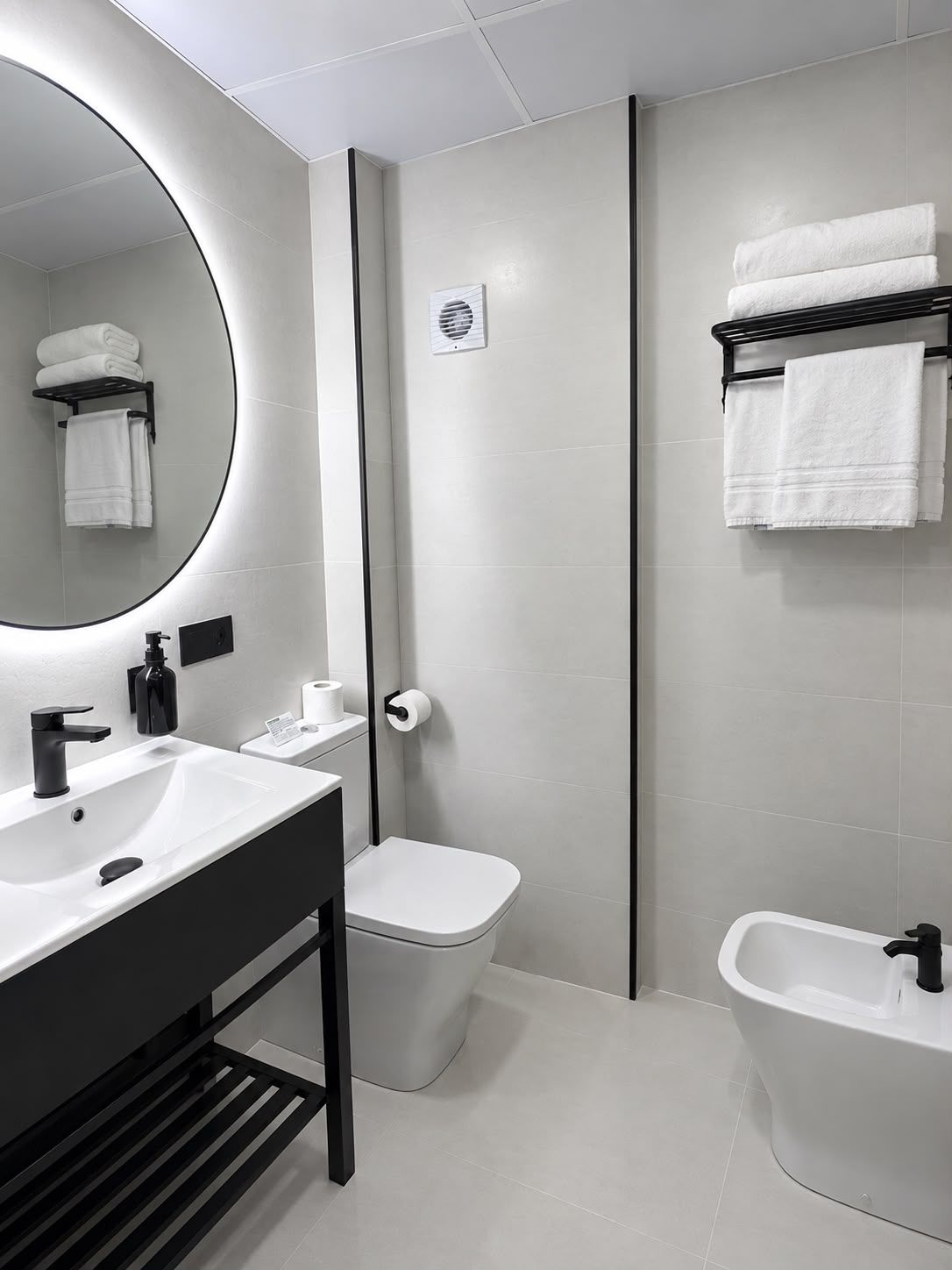 Un baño moderno con un espejo redondo, un lavamanos blanco, un inodoro y un bidé.