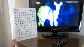 Un televisor con control remoto, guía de canales de televisión y una mesa de vidrio.