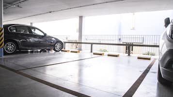 Un garaje para estacionamiento con dos autos estacionados, piso de concreto y una barandilla con pequeños maceteros.