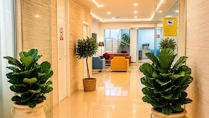 Entrada de un hotel con un letrero que dice 'HOTEL', una recepción y plantas en macetas.
