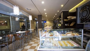 Un expositor de pastelería con diversos pasteles y un área de estar con sillas y mesas.