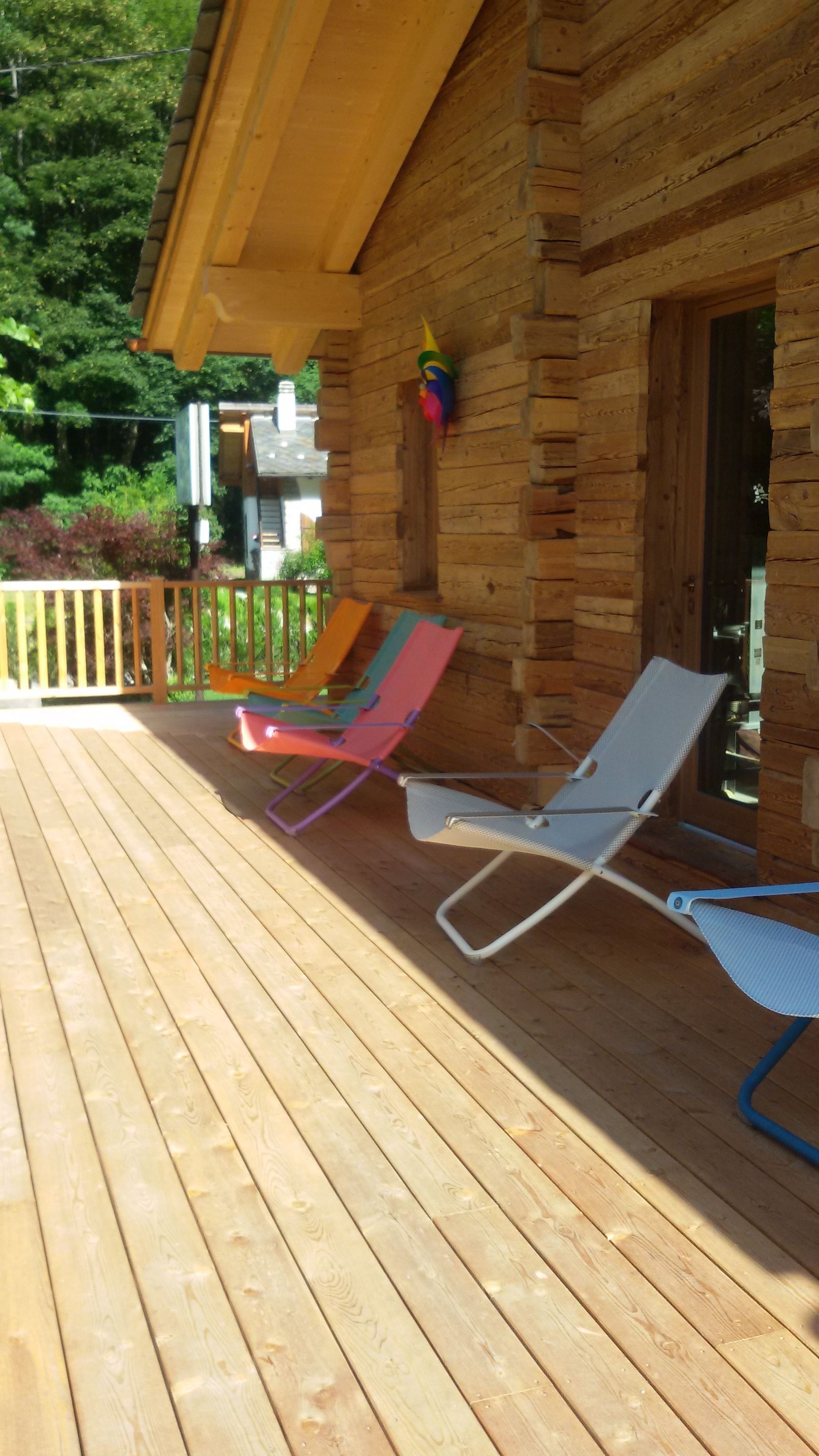 A wooden deck with two lounge chairs and a colorful birdhouse.