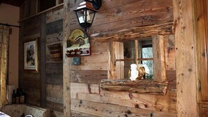 Interior rústico de una cabaña de madera con pared de madera, un farol, un cuadro enmarcado y un ventanal con un adorno.