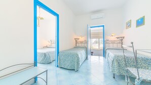 A room with two single beds, a small table, and a chair. There is a window with a view of the outside. - Hotel Celeste (Procida)