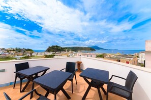 A terrace with four dark tables and chairs, overlooking a coastal town and the sea. - Hotel Celeste (Procida)