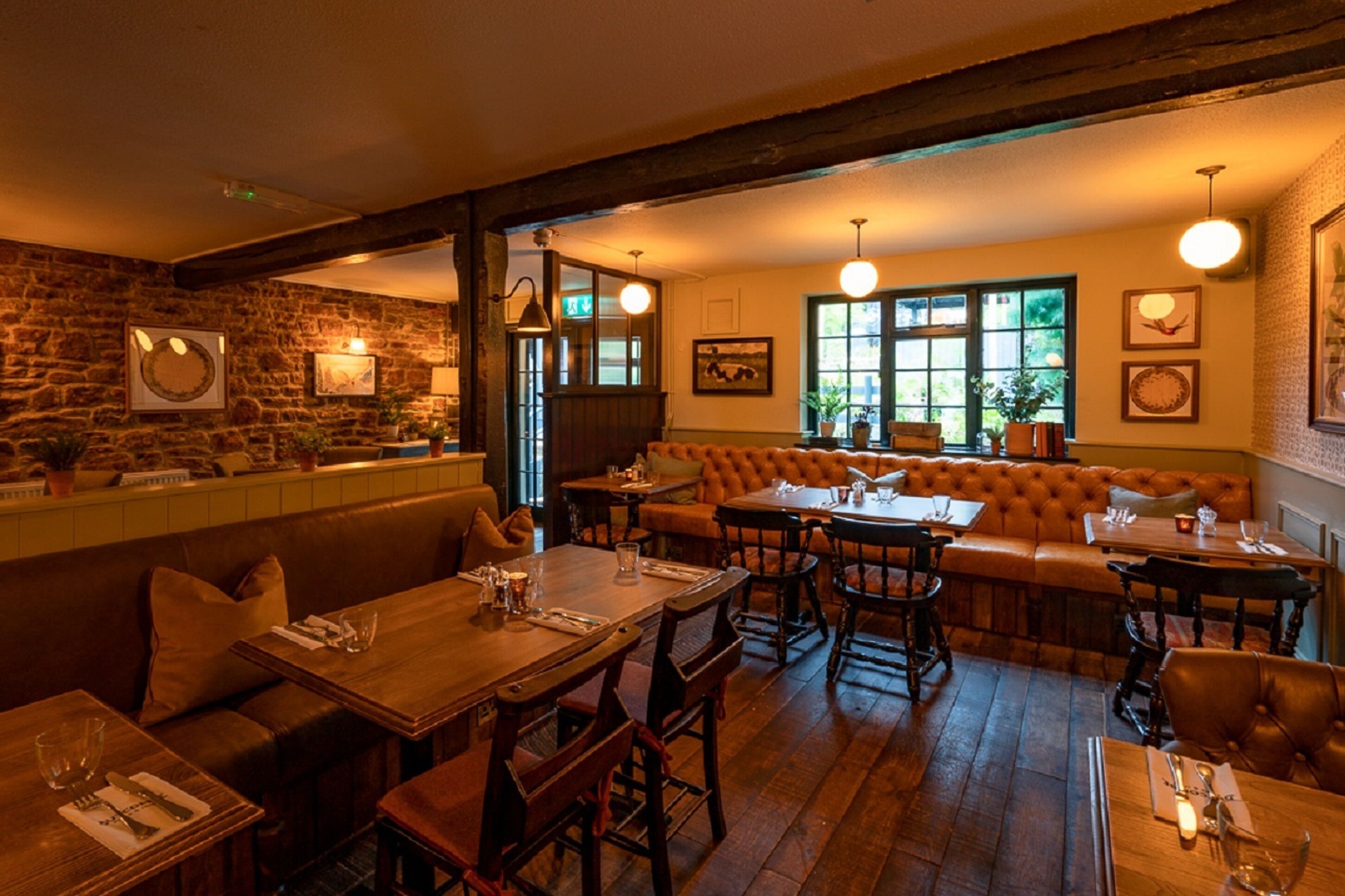 Ein gemütliches Restaurant mit Holztischen und -bänken, Steinwänden und großen Fenstern.
