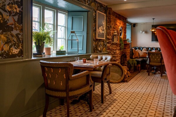 A dining area with a wooden table and chairs, a stone wall, and a view through a window with a blue door. - Ring O Bells (Bristol)