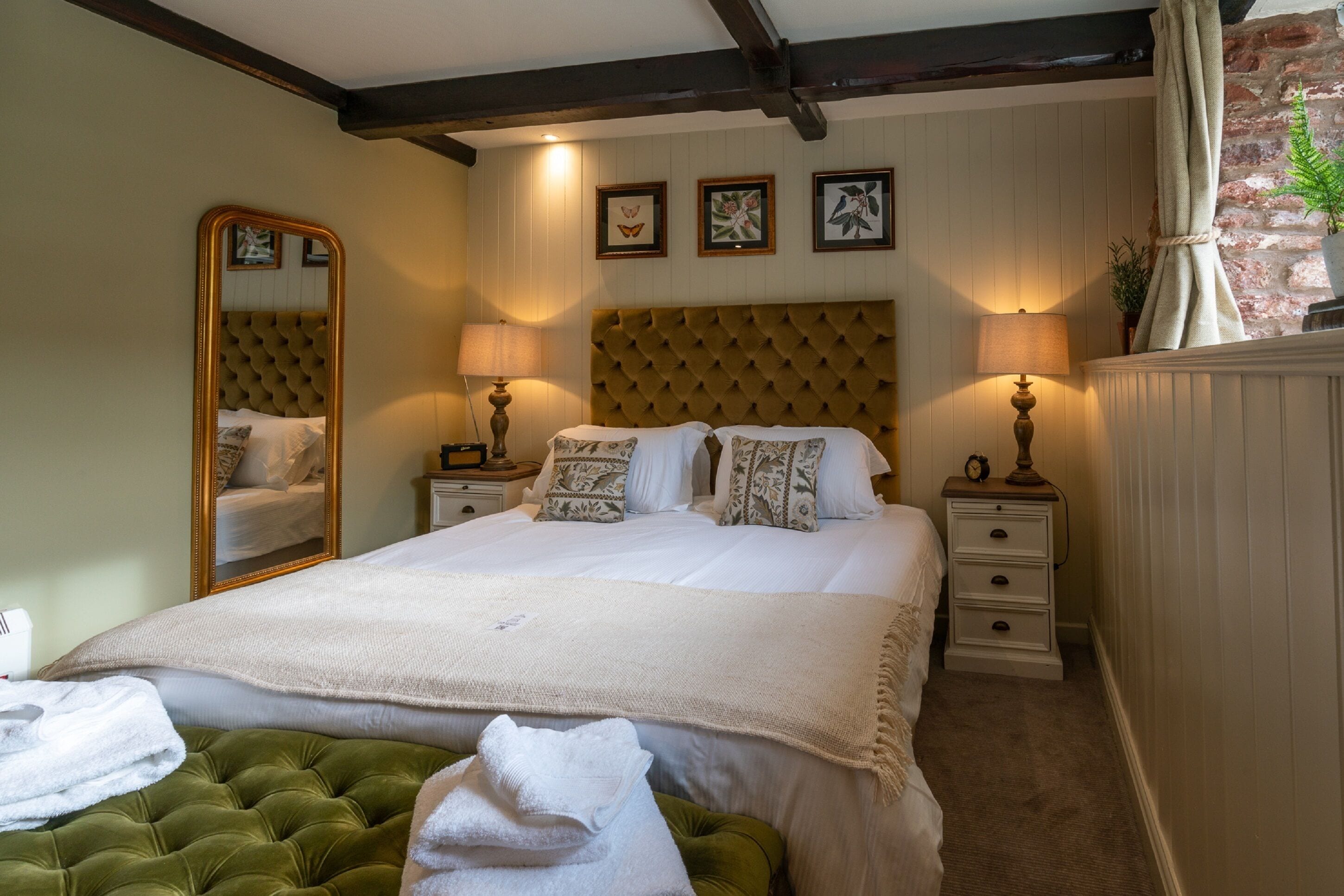 Habitación de hotel con una cama grande, dos mesitas de noche, un espejo y un banco tapizado en verde.