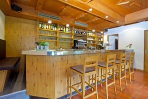 A wooden bar area with shelves of bottles and glasses, a counter, and bar stools. - FamilyHotel Stegerhaus (Valle Aurina)