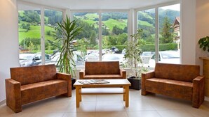 Ein Zimmer mit zwei Sofas und einem Couchtisch, große Fenster mit Blick auf grüne Hügel und geparkte Autos.