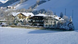 Ein schneebedecktes Berghotel mit mehreren Gebäuden, eine Skipiste im Hintergrund und ein klarer Himmel.
