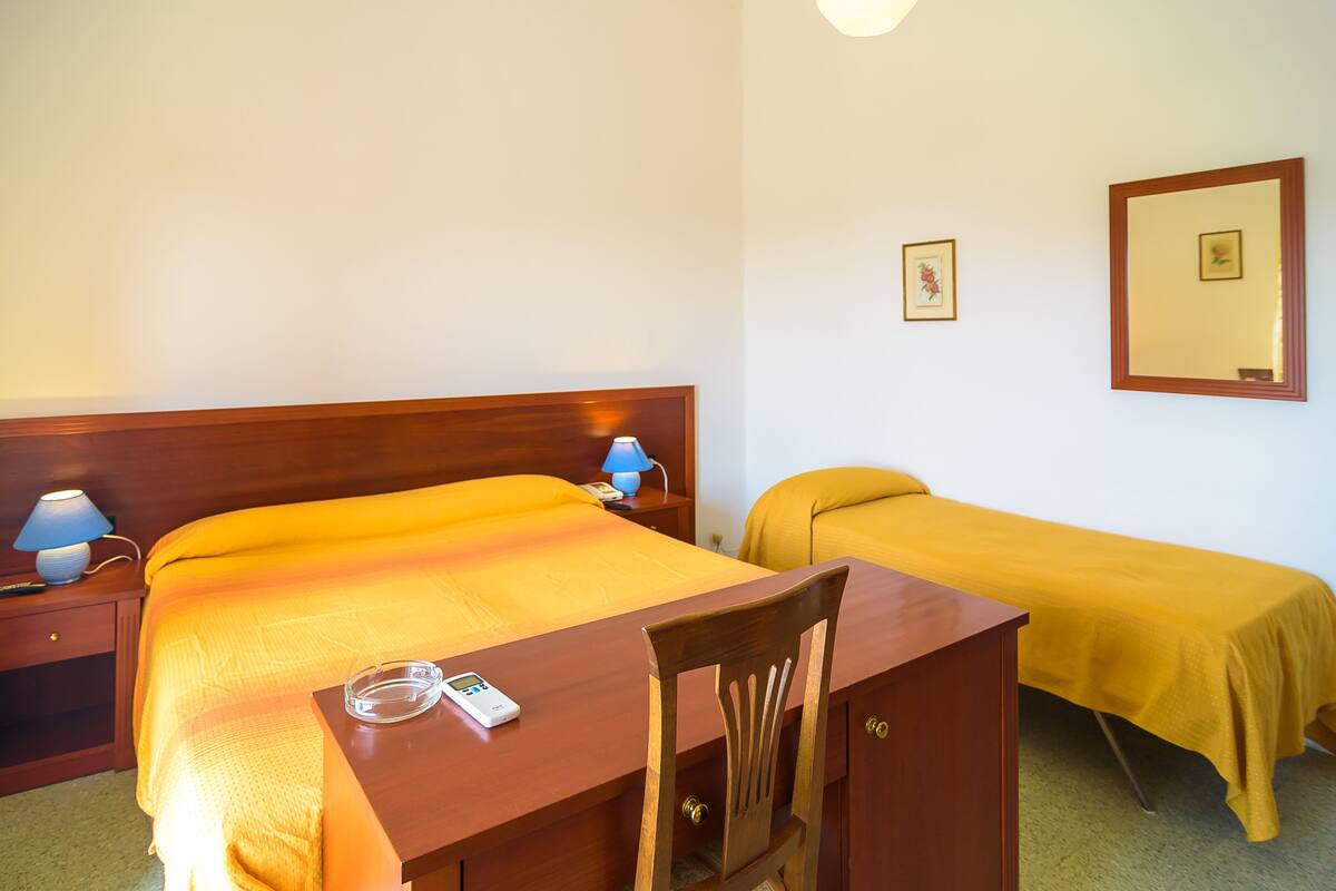 Ein Hotelzimmer mit einem hölzernen Bett, einem Schreibtisch mit Stuhl, einer Nachttischlampe und einem Telefon am Nachttisch.