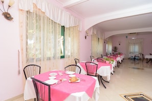A dining area with pink tablecloths, white chairs, and a long table with plates and cutlery.