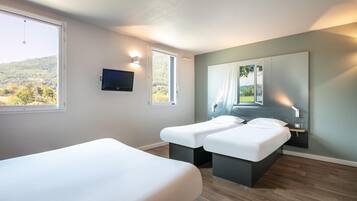 A modern hotel room with two beds, a large window with a view of a forest, a mounted TV, and a mirror reflecting the window view.