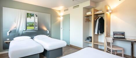 Une chambre d’hôtel moderne dotée d’un grand lit, d’un bureau avec un ordinateur portable, d’une chaise, d’une armoire et offrant une vue sur la verdure environnante.