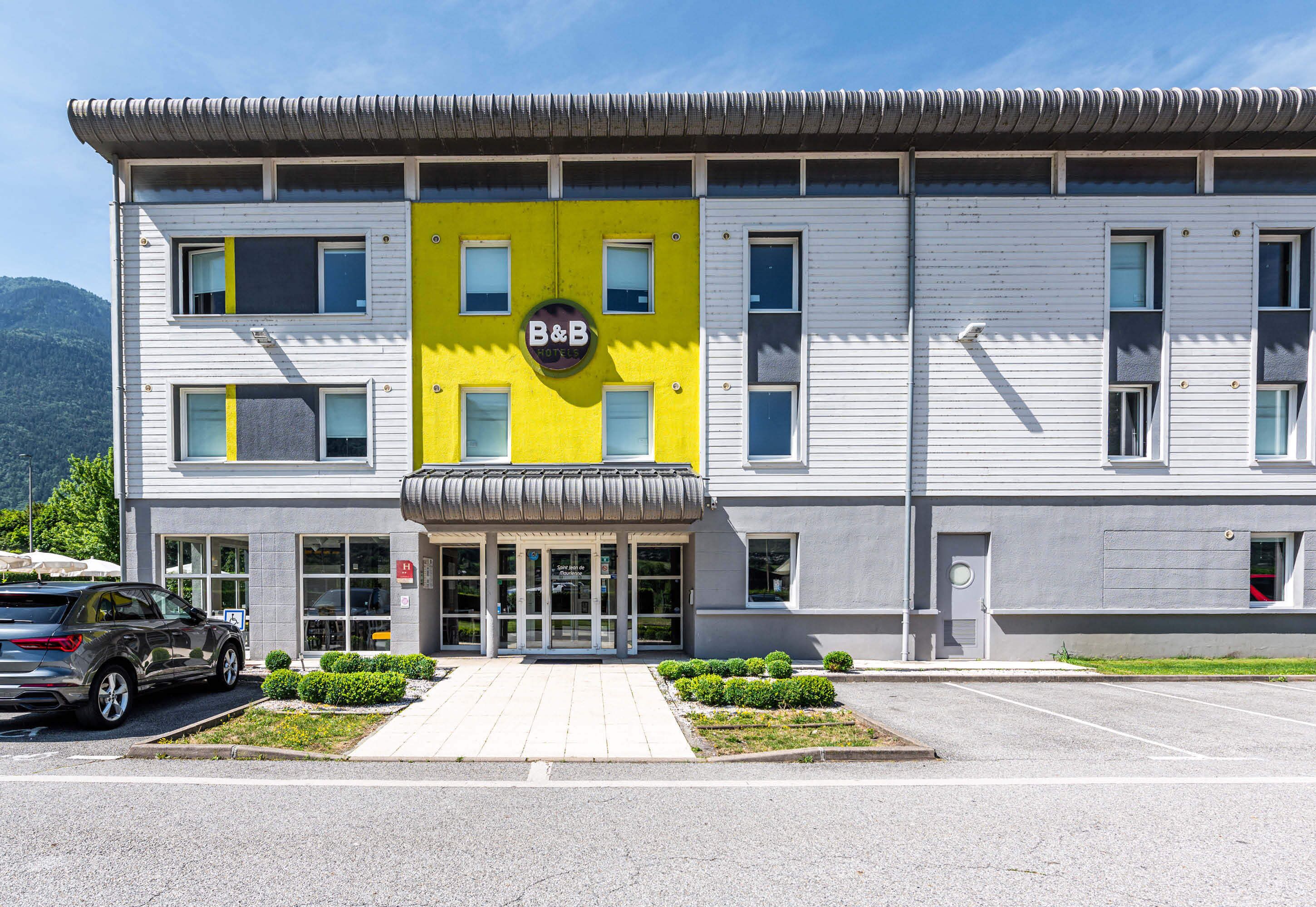 A two-story building with a yellow and white facade, featuring a large sign with "B&B" and a logo.