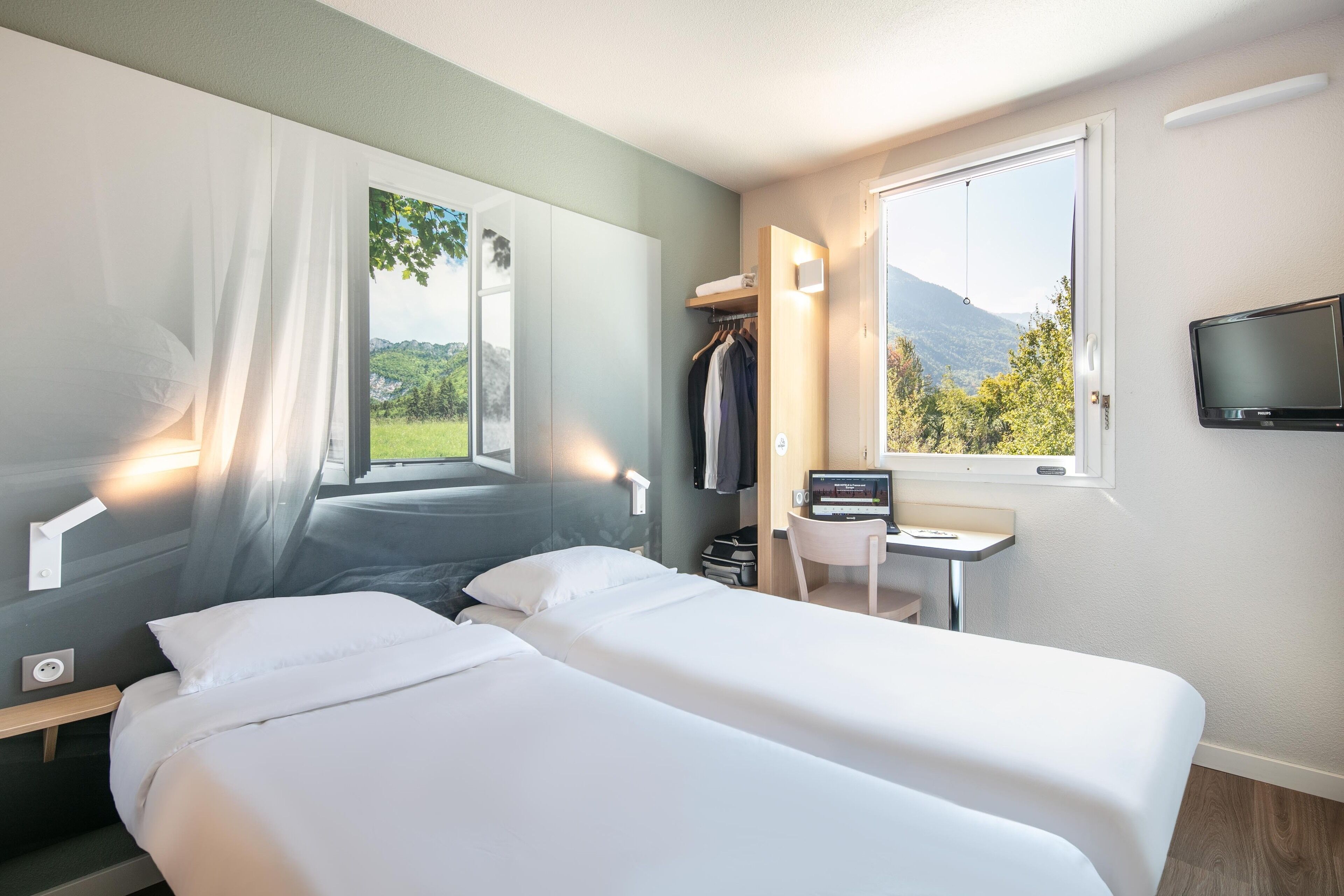 Une chambre d’hôtel équipée d’un lit, d’un bureau, d’une télévision et d’une fenêtre donnant sur la montagne.