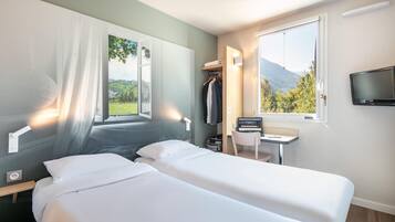 Une chambre d’hôtel équipée d’un lit, d’un bureau, d’une télévision et d’une fenêtre donnant sur la montagne.