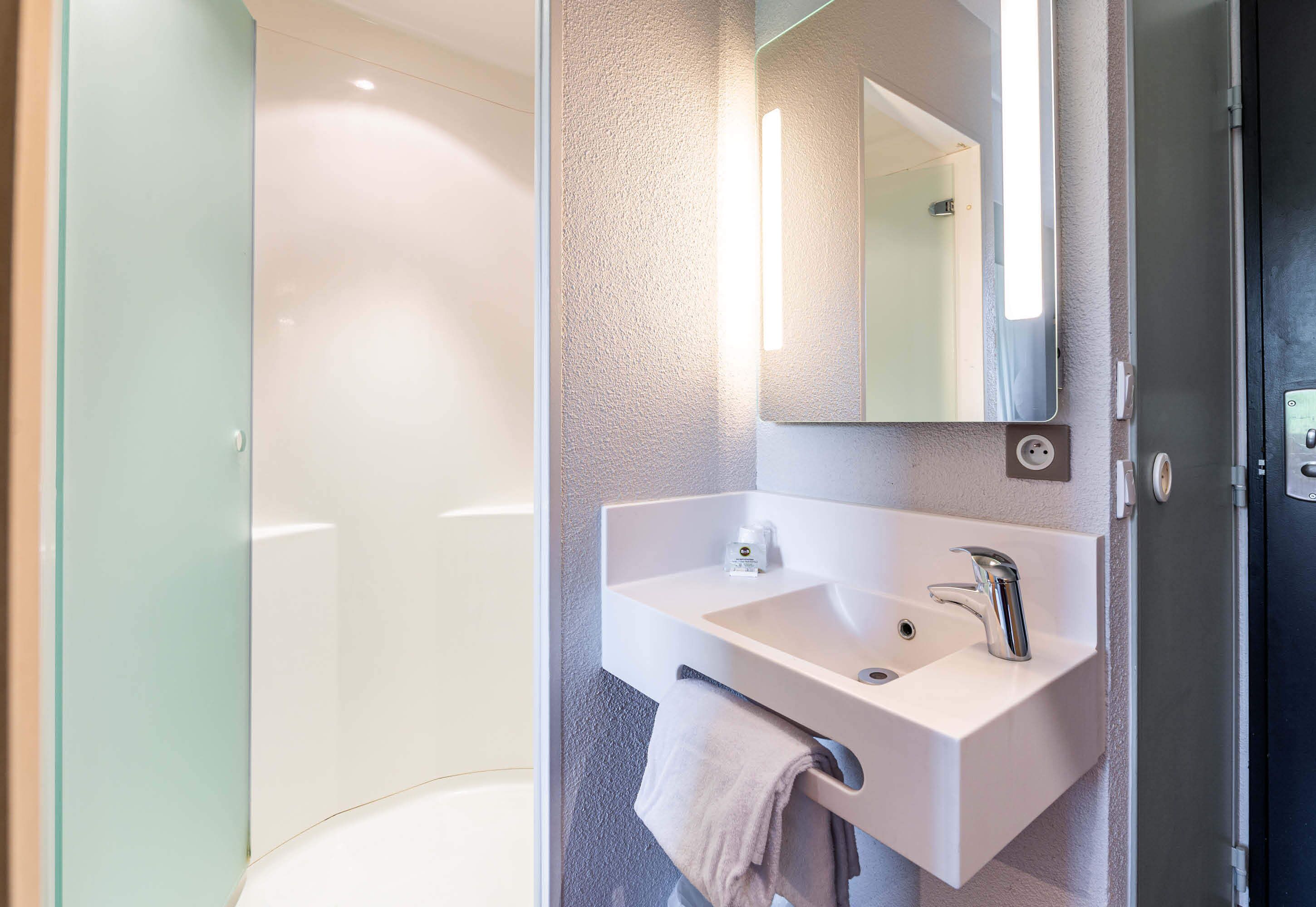 Een moderne badkamer met een witte wastafel, een spiegel en een handdoek aan een rek.