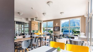 Una cafetería moderna con varias mesas y sillas, amplias ventanas con vista a la montaña y un interior limpio y luminoso.