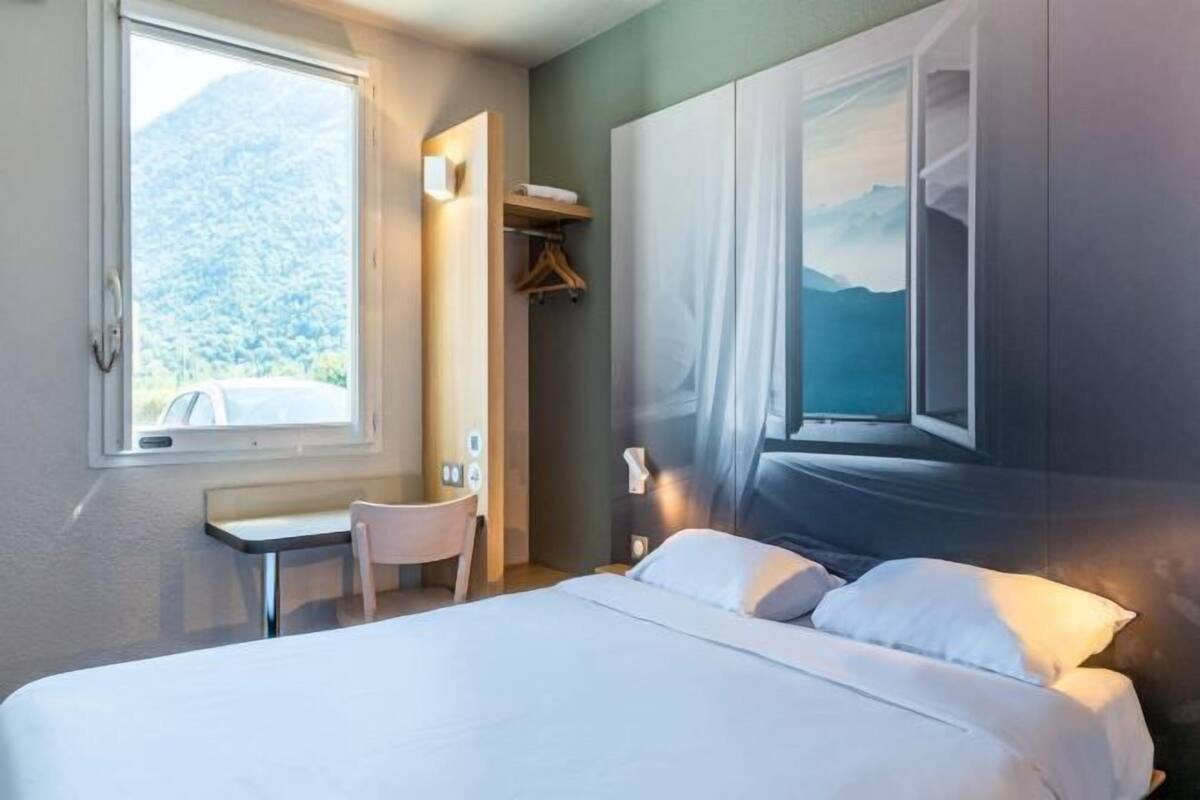 Ein Schlafzimmer mit Bett, Schreibtisch, Stuhl und Fenster mit Bergblick.