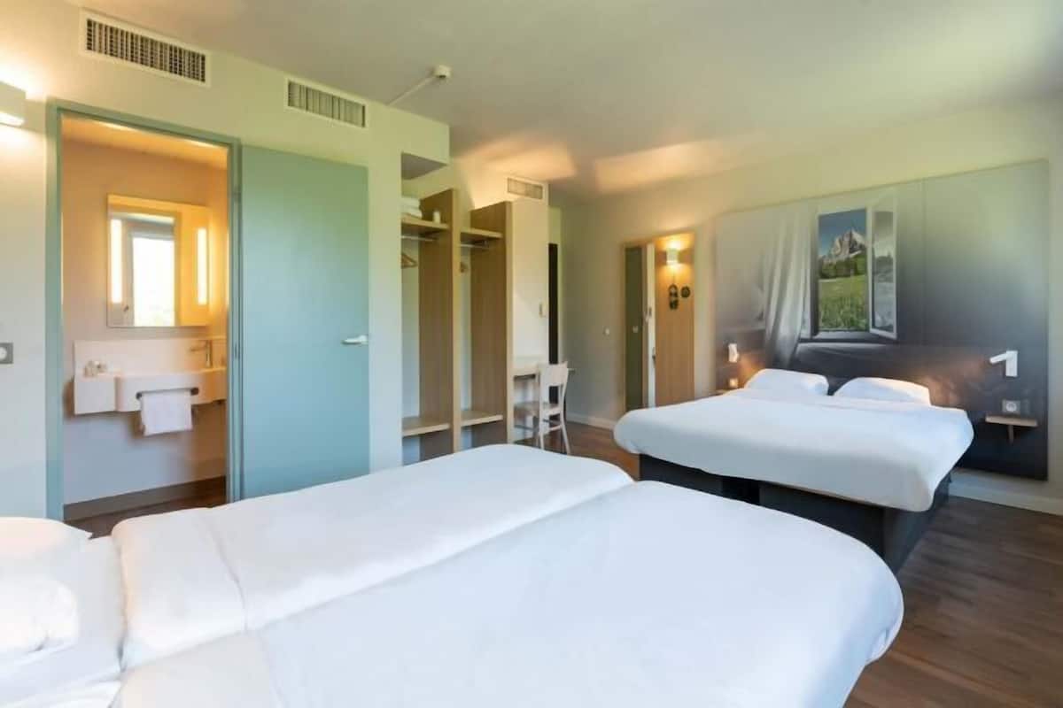 Ein Hotelzimmer mit zwei Betten, einem Badezimmer inklusive Spiegel und Blick auf eine Landschaft durch ein Fenster.