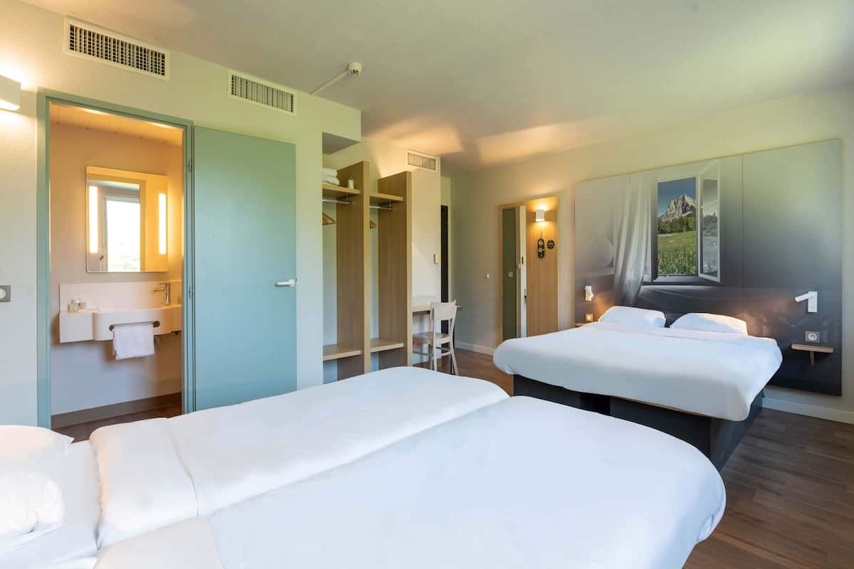 Ein Hotelzimmer mit zwei Betten, einem Badezimmer mit Spiegel und Blick auf einen Berg durch ein Fenster.