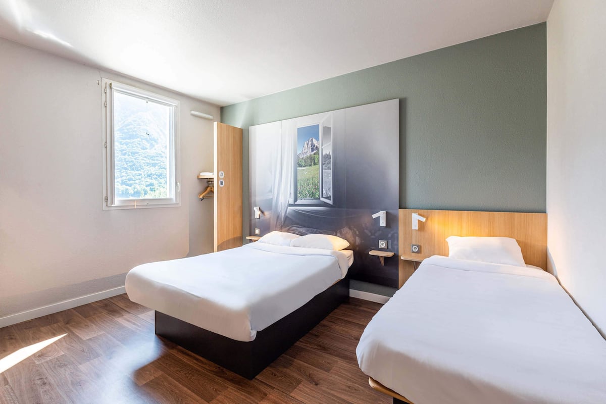 Ein modernes Hotelzimmer mit zwei Betten, Holzboden, einem großen Fenster und einem Wandbild.