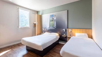 A modern hotel room with two beds, wooden flooring, a large window, and a wall-mounted artwork.