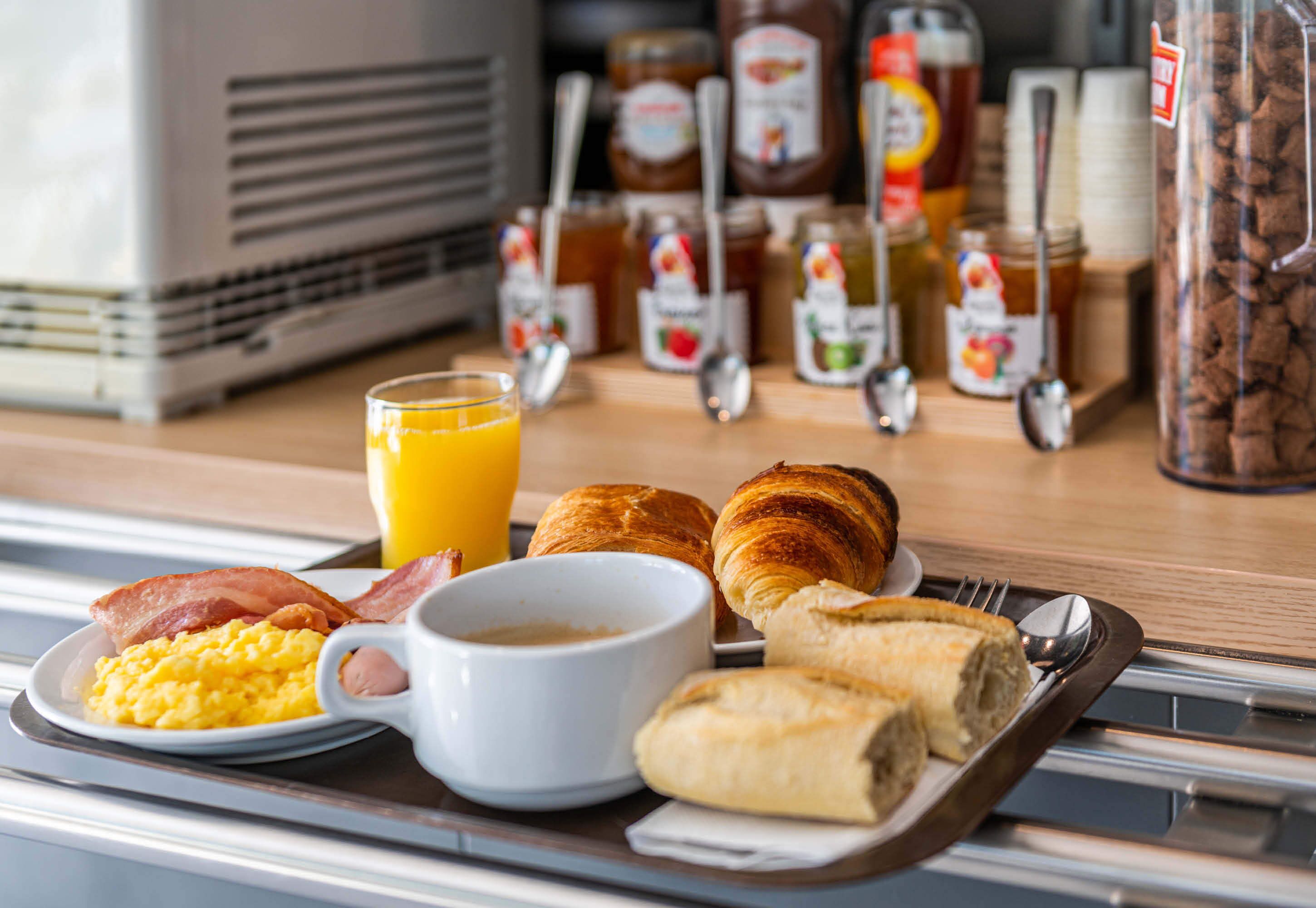 A breakfast tray with scrambled eggs, bacon, croissants, a glass of orange juice, and a cup of coffee.