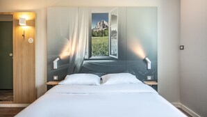 Un dormitorio con cama, mesita de noche, luz de pared y puerta.