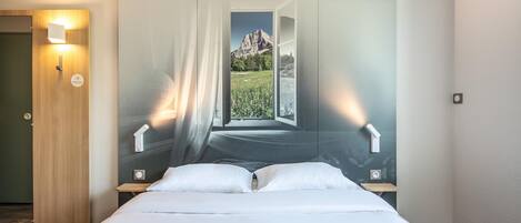 Un dormitorio con cama, mesita de noche, luz de pared y puerta.