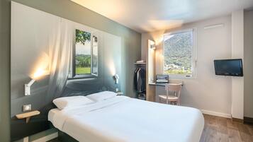 Une chambre d’hôtel moderne dotée d’un grand lit, d’un bureau avec une chaise, d’une télévision et offrant une vue sur un paysage montagneux.