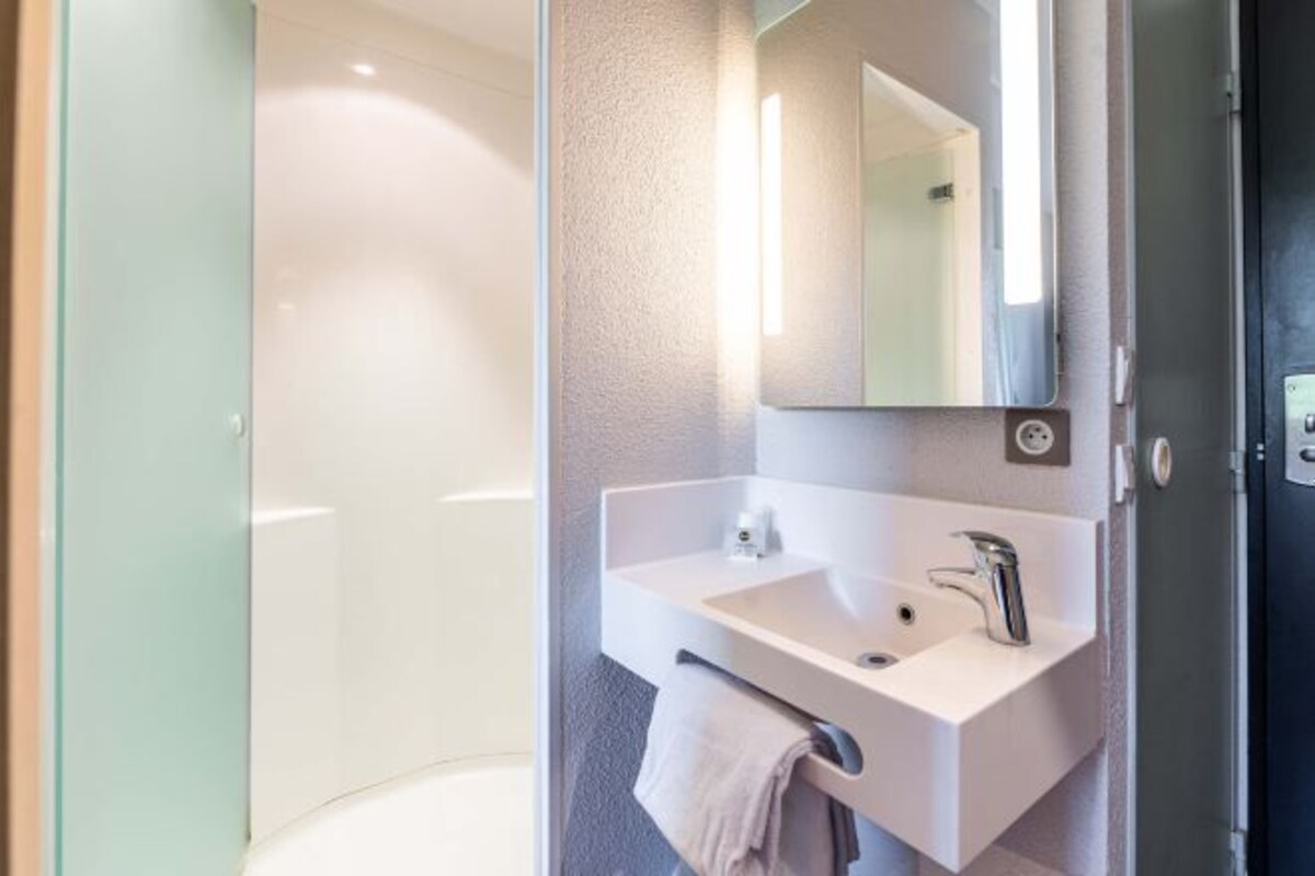 A modern bathroom with a glass shower enclosure, a white sink with a mirror, and a towel hanging on the wall.