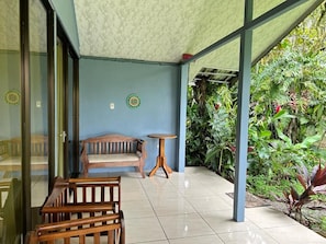 A covered outdoor seating area with a bench and a small table, surrounded by lush greenery. - Hotel B&B Garden Grecia (San Jose)