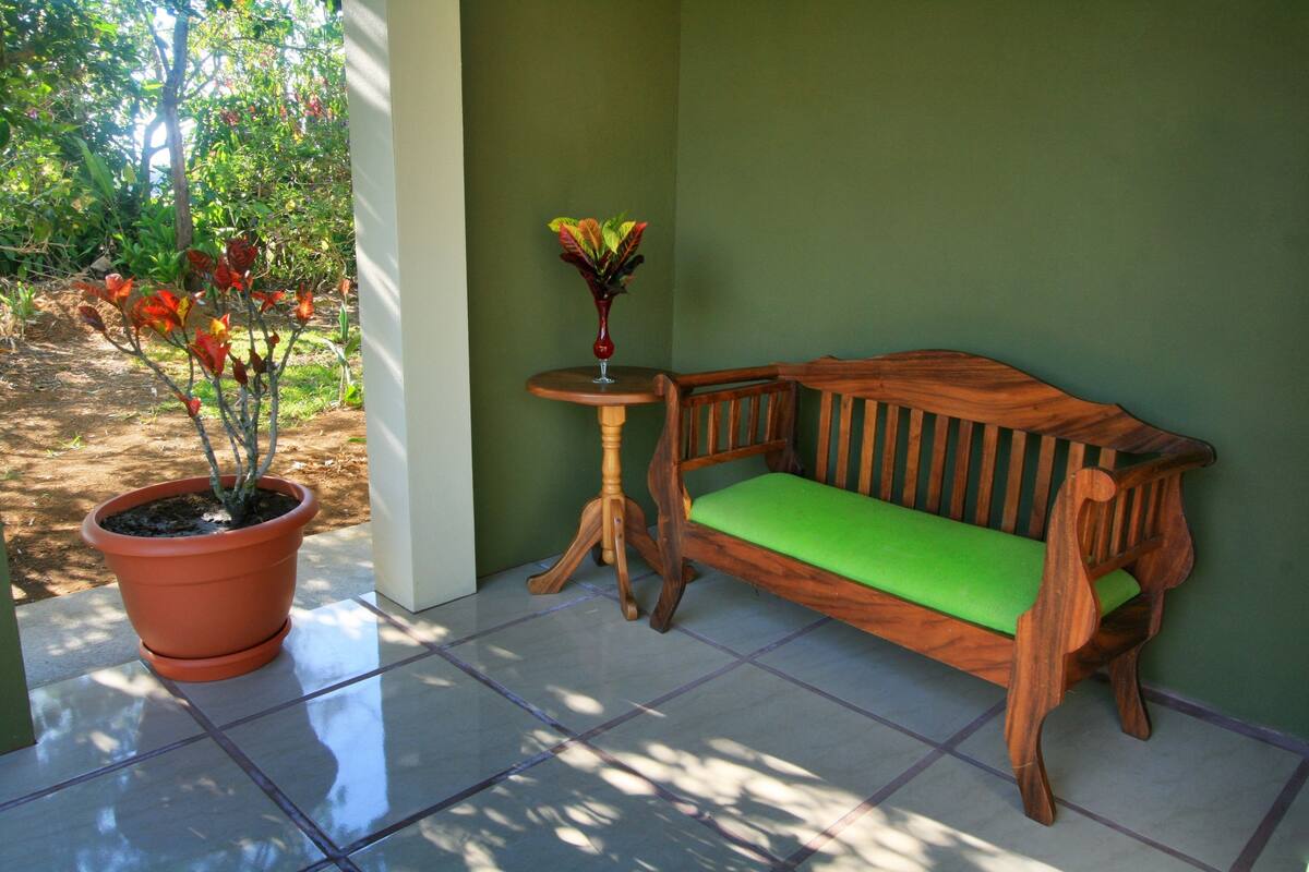 Un banco de madera con un cojín verde, una planta en maceta y una mesita redonda.